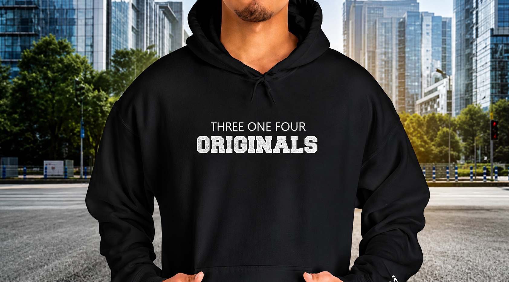 A man wearing a black pullover hoodie with the text 'THREE ONE FOUR ORIGINALS' printed in white on the chest, set against a blurred city street background.